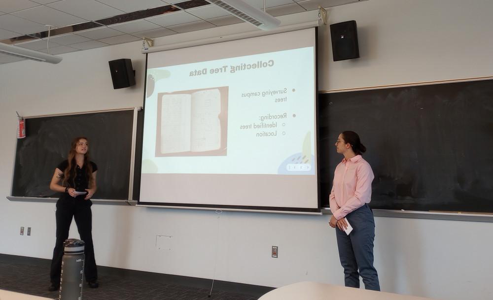 two students standing in the front of the room presenting slides